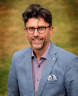 A portrait shot of a friendly man with dark curly hair and glasses.