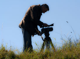 A man with a video camera on a field can be seen here