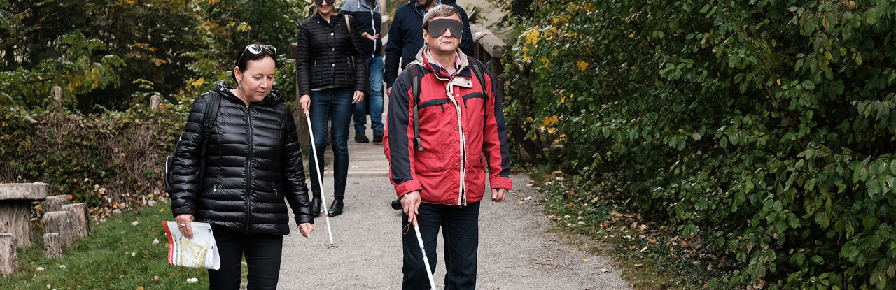 Członkowie zespołu projektu próbują posługiwać się sprzętem dla niewidomych. Osoby spacerują w parach. Jedna z nich ma zasłonięte oczy i posługuje się białą laską, druga osoba asystuje i pilnuje bezpieczeństwa.